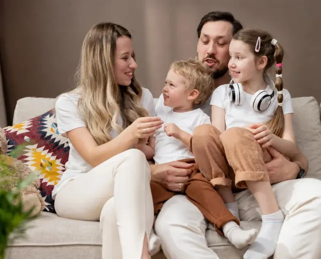 Happy family of four sitting together on a light sofa in a bright living room